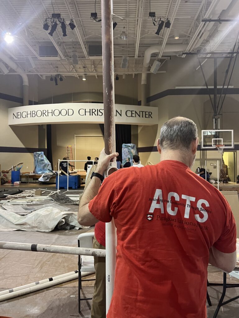 A Paragon Bank employee measures a length of pipe being used to build a frame of a faux hut.